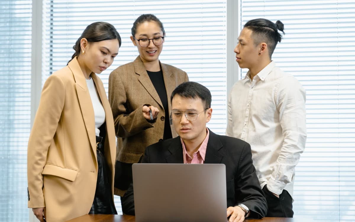 Bốn đồng nghiệp đứng quanh một chiếc laptop, cùng xem và bàn về kết quả trên màn hình