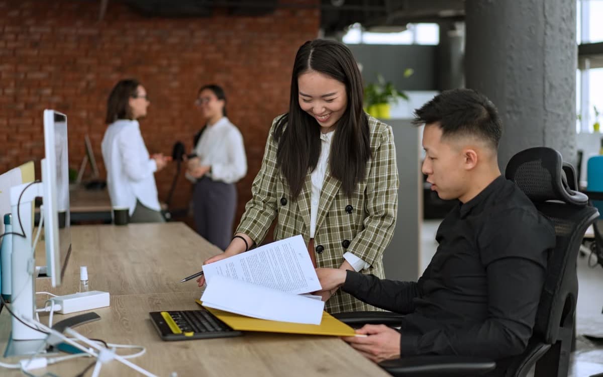Hai đồng nghiệp cùng xem một tập tài liệu tại bàn làm việc