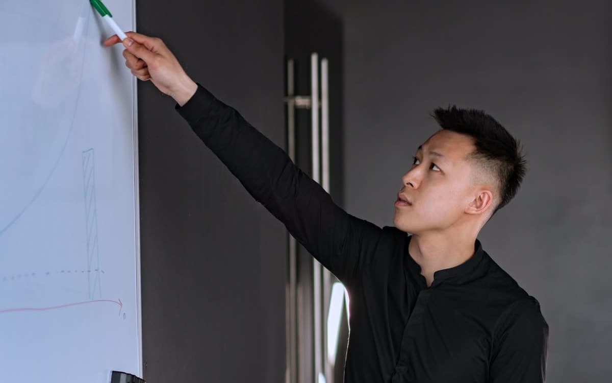 Một người đứng trước bảng trắng, tay chỉ vào biểu đồ đang vẽ dở