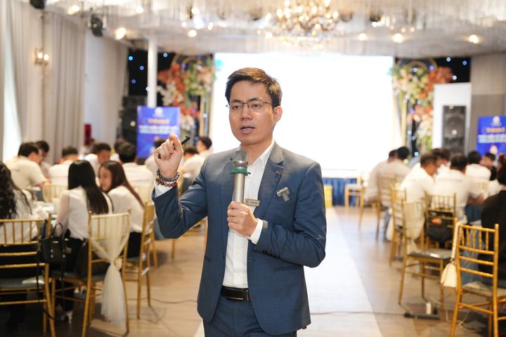 Diễn giả cầm micro giữa hội trường, phía sau là màn chiếu