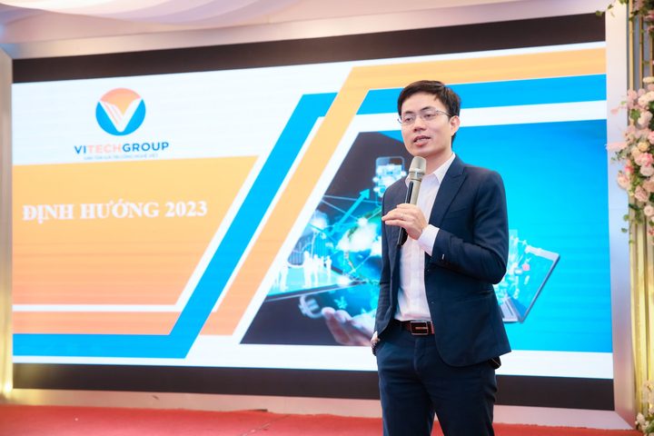 Diễn giả cầm micro trên sân khấu có màn hình trình chiếu