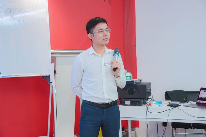 Diễn giả cầm micro đứng cạnh bảng trắng