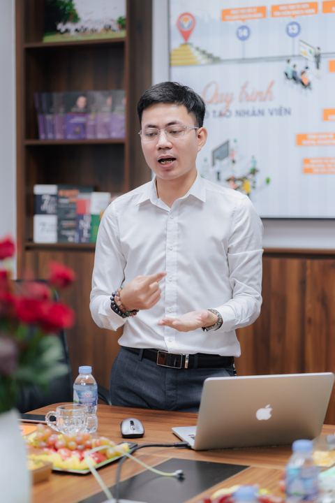 Diễn giả chia sẻ trong phòng họp, phía sau là kệ sách