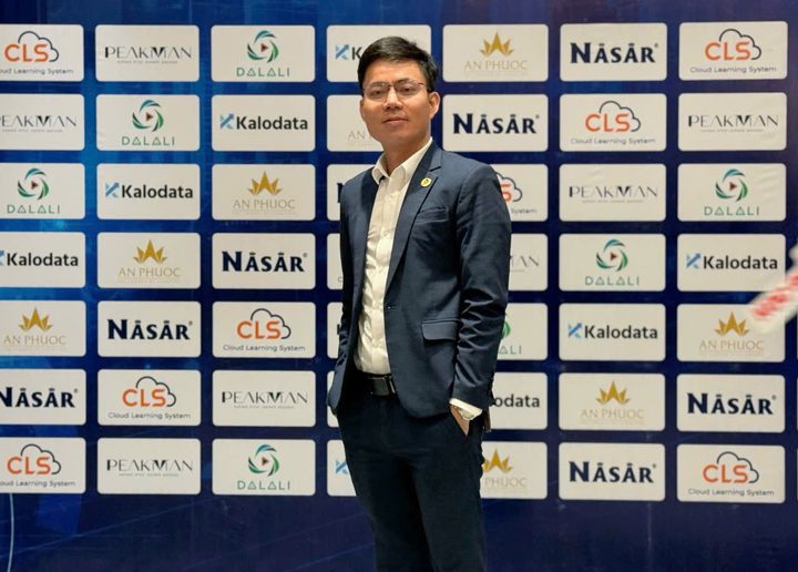 Chân dung chụp tại sự kiện, phía sau là phông logo đối tác