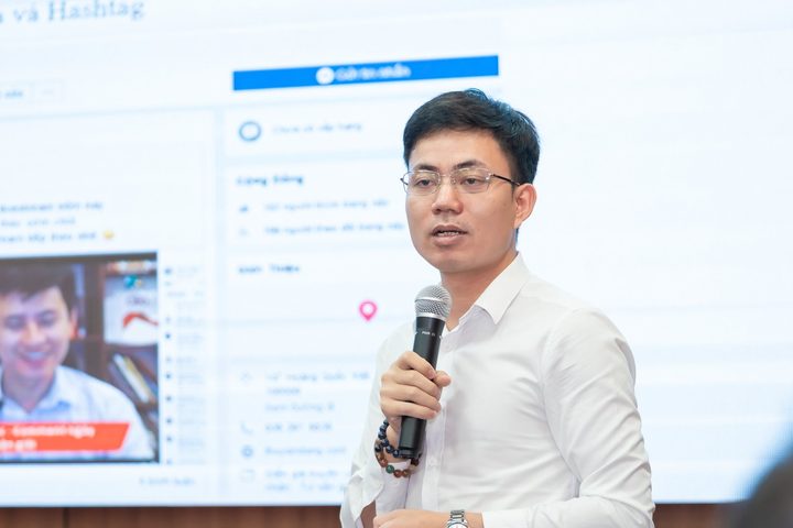 Diễn giả cầm micro chia sẻ trước màn hình lớn